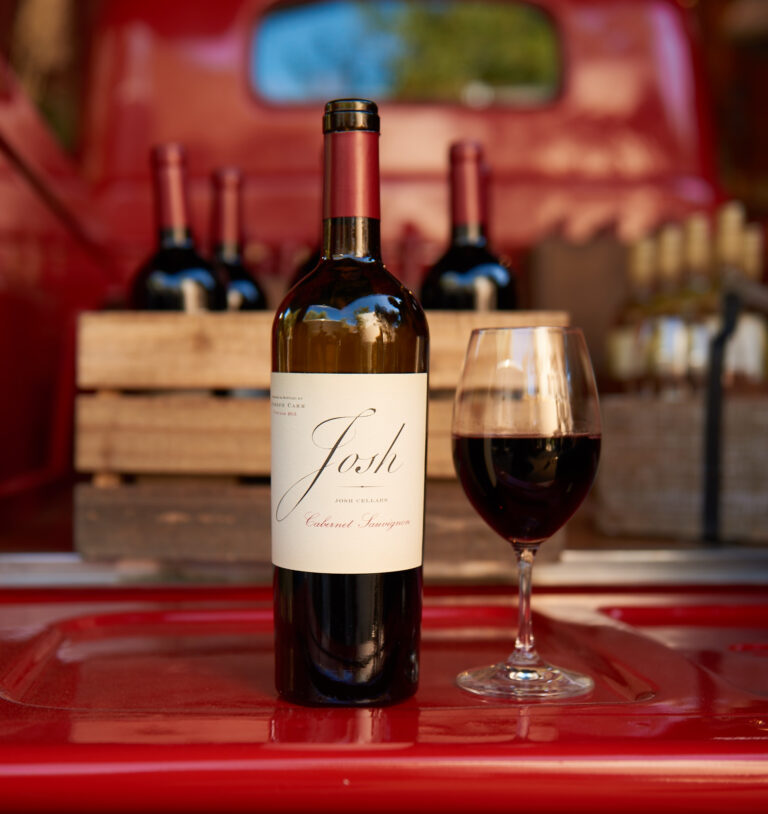 A bottle of Cabernet Sauvignon and a glass of wine on the back of a red pickup truck